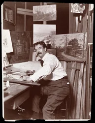 Portrait of Ernest Gross, scenic designer, sitting in his studio at his drafting table, 1908-9